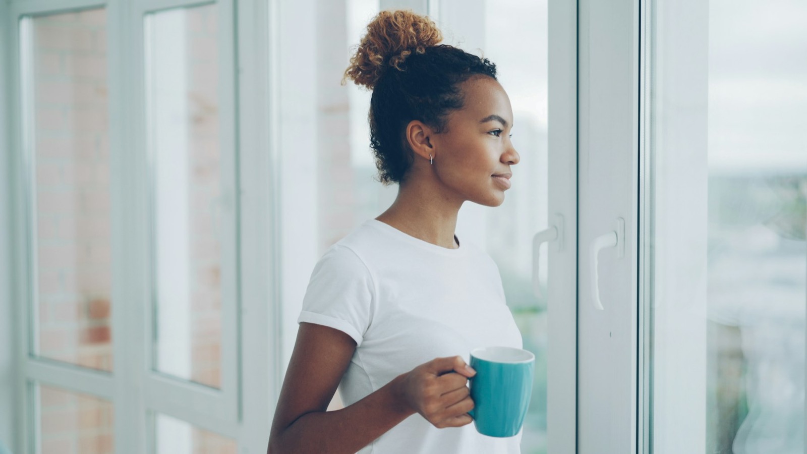 A woman at a bright window in the morning, holding a mug of tea