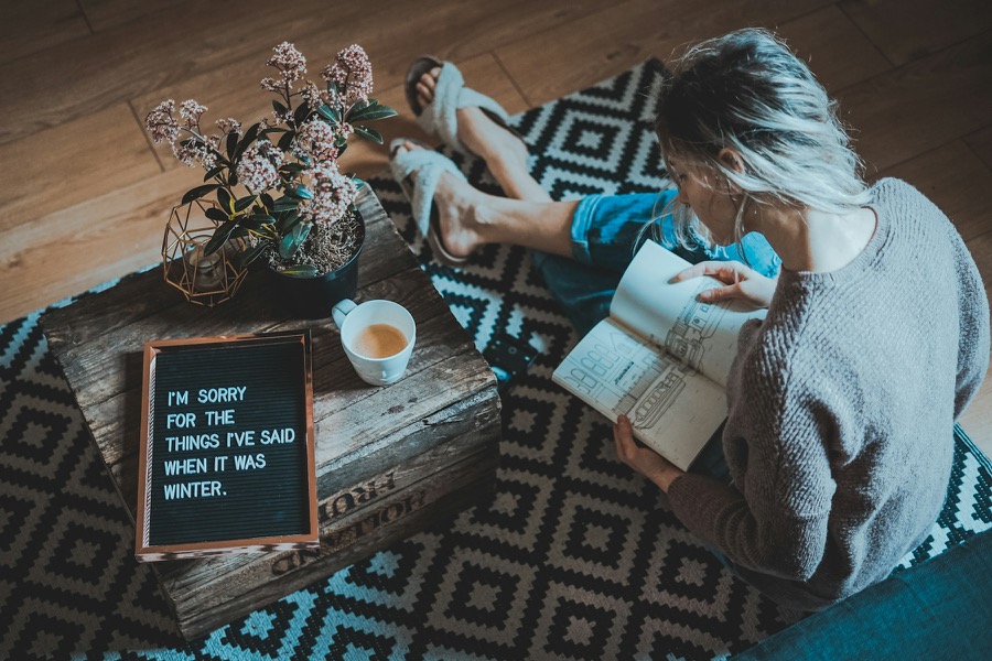 A woman reading on a patterned rug beside a coffee table