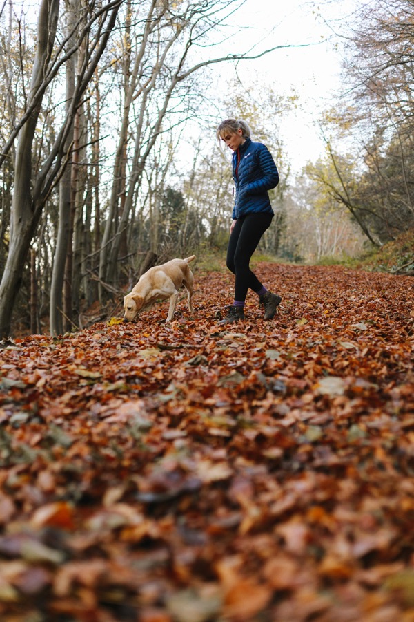 A woman walking a dog along a path covered in autumn leaves